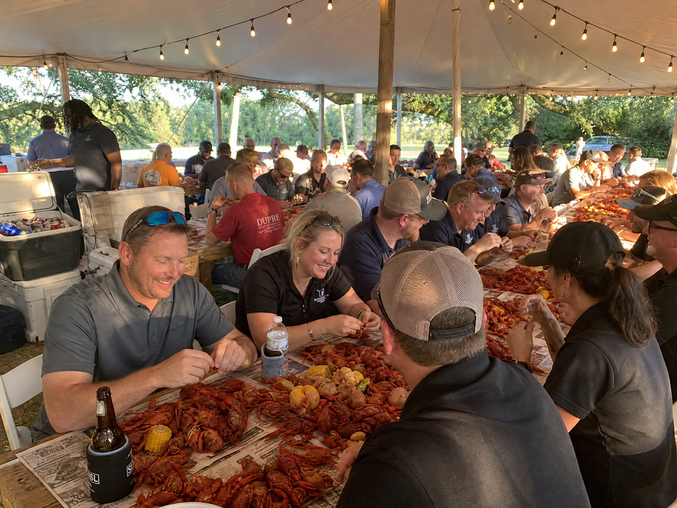 Corporate crawfish boil under large event tent with coworkers eating at crawfish tables
