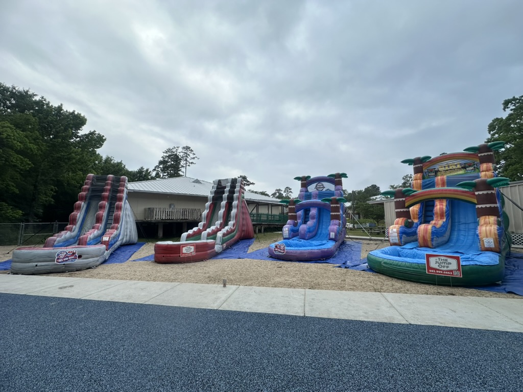 Four water slides set up side by side on blue tarps for Woodlake Elementary water day